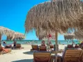 Słoneczne rumuńskie plaże z drewnianymi leżakami i strzechowymi parasolami. W tle widać ludzi kąpiących się w morzu.