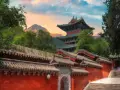 Zachód słońca nad klasztorem Shaolin. Czerwone mury, zielone dachy i majestatyczne góry tworzą malowniczy krajobraz.
