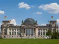 Imponujący Reichstag z charakterystyczną szklaną kopułą, otoczony zielonym trawnikiem i błękitnym niebem z chmurami.