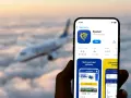 Ręka trzyma smartfon z aplikacją Ryanair, gotową do odprawy online. W tle widać samolot lecący wśród chmur.
