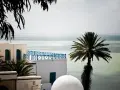 Białe budynki z niebieskimi okiennicami i balustradą, palma i morze. Czy Tunezja jest bezpieczna? Widok sugeruje spokój i piękno.