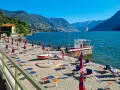 Plaże nad jeziorem Como, z rzędami leżaków i parasoli, zapraszają do relaksu. W tle góry i błękitne niebo.