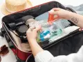 Ręce pakują kosmetyki w przezroczystej kosmetyczce do czerwonej walizki.