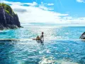 Madera, listopad. Słoneczna pogoda zachęca do kąpieli w basenie z widokiem na ocean. Kobieta w białym bikini relaksuje się na brzegu.