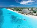 Widok na turkusowe morze i białą plażę z hotelami, kiedy na Zanzibarze. Łódź motorowa z pasażerami płynie po wodzie.
