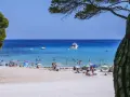 Baleary jakie wyspy? Słoneczna plaża z turkusową wodą, łodziami i ludźmi odpoczywającymi pod parasolami.