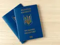 Dwa niebieskie paszporty biometryczne Ukrainy z złotym godłem i napisami leżą na drewnianym blacie.