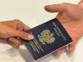 Dłoń przekazuje ciemnoniebieski paszport polski z godłem orła. Dokument podróży gotowy do przekroczenia granicy.