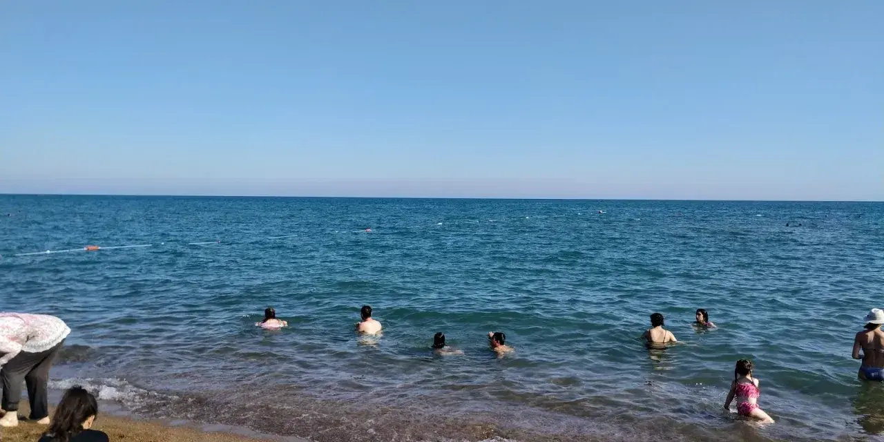 Słoneczny dzień na plaży Lara. Ludzie kąpią się w turkusowym morzu, inni odpoczywają na piaszczystym brzegu.