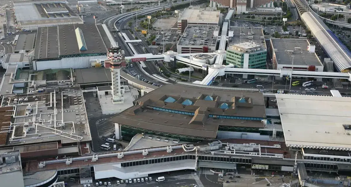 Widok z lotu ptaka na lotnisko Rzym Fiumicino. Widoczne terminale, wieża kontroli lotów, drogi kołowania i parkingi.