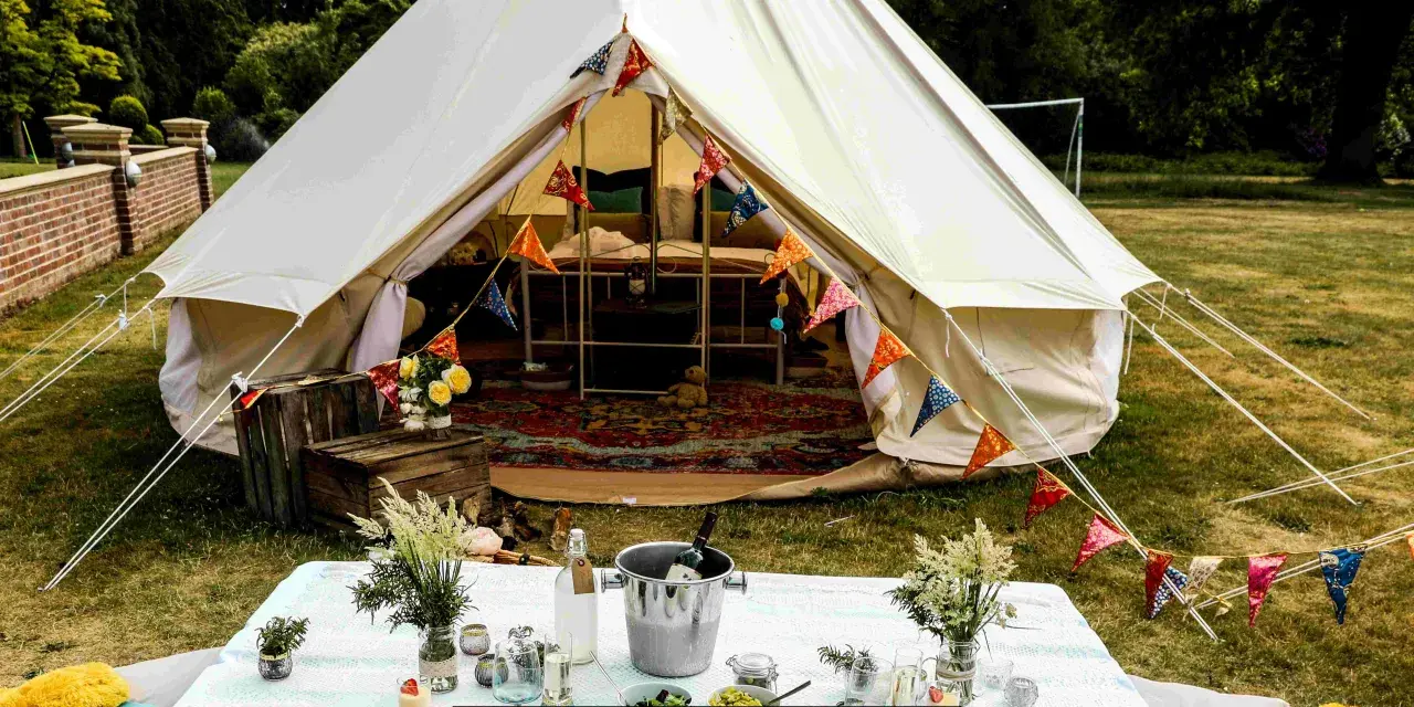 Idealne miejsce na glamping: namiot typu bell z kolorowymi chorągiewkami, stół z winem i kwiatami.