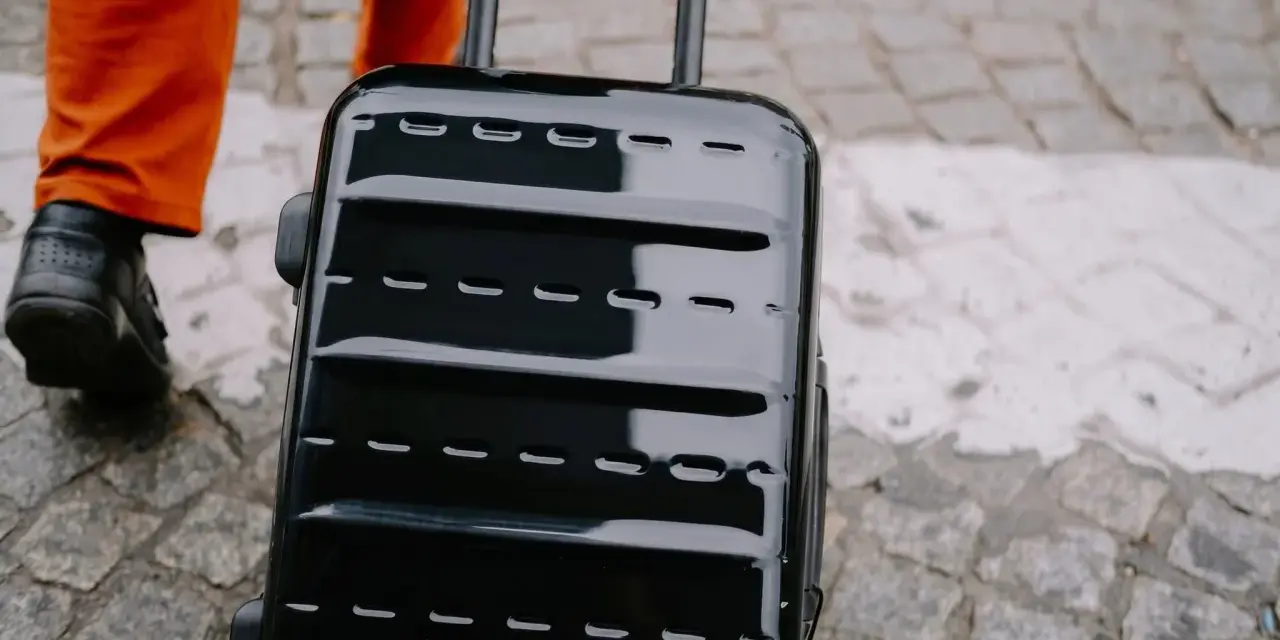 Błyszcząca, czarna walizka, idealna jako bagaż podręczny Ryanair, ciągnięta po bruku.