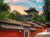 Zachód słońca nad klasztorem Shaolin. Czerwone mury, zielone dachy i majestatyczne góry tworzą malowniczy krajobraz.