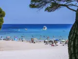 Baleary jakie wyspy? Słoneczna plaża z turkusową wodą, łodziami i ludźmi odpoczywającymi pod parasolami.
