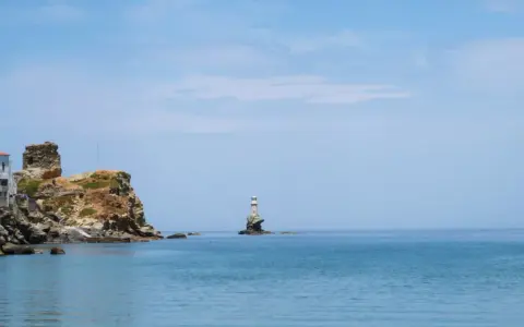 Widok na morze z latarnią morską na skale i zabudowaniami na klifie na wyspie Andros.
