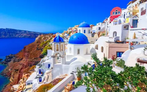 Santorini wakacje: białe domy z niebieskimi kopułami na zboczu klifu nad lazurowym morzem. Idealne miejsce na wymarzone wakacje.