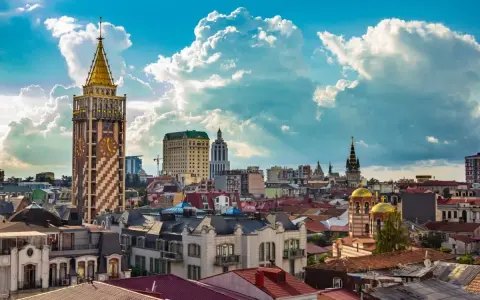 Widok na stolicę Adżarii, Batumi, z charakterystyczną wieżą zegarową i złotymi kopułami cerkwi pod błękitnym, chmurowym niebem.