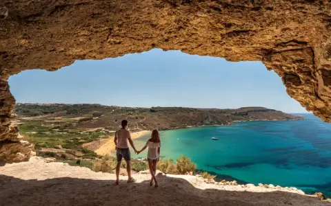 Para zakochanych podziwia widok na turkusowe morze i plażę z jaskini. Malta w styczniu pogoda idealna na spacer.