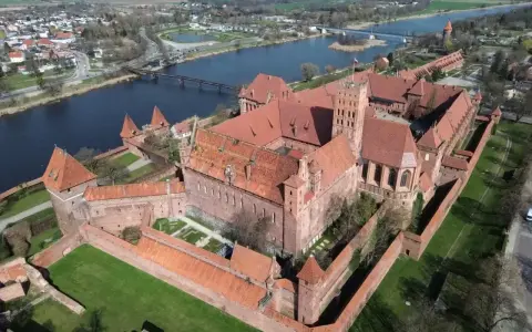 Potężny zamek z czerwonej cegły, największy zamek w Europie, otoczony murami obronnymi, nad rzeką.