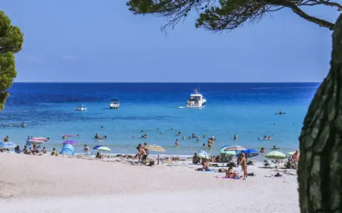 Baleary jakie wyspy? Słoneczna plaża z turkusową wodą, łodziami i ludźmi odpoczywającymi pod parasolami.