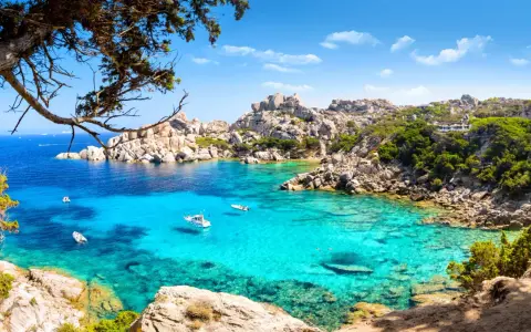 Turkusowa zatoka Costa Smeralda z łodziami i skalistym wybrzeżem.