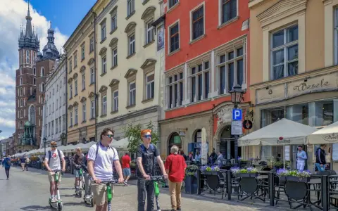 Młodzi ludzie na hulajnogach w Krakowie, idealne na city break. W tle Sukiennice i Kościół Mariacki.