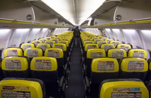 Puste rzędy żółtych siedzeń w samolocie Ryanair. Widać instrukcje bezpieczeństwa na oparciach.