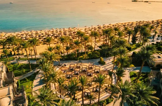 Rajska plaża w Makadi Bay z rzędami leżaków i palm. W oddali błękitne morze i statki.