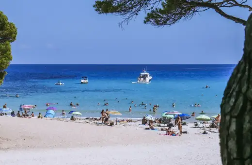 Baleary jakie wyspy? Słoneczna plaża z turkusową wodą, łodziami i ludźmi odpoczywającymi pod parasolami.