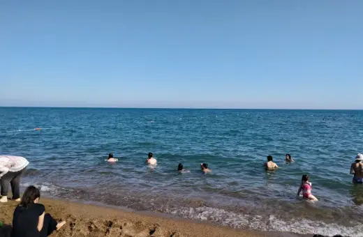 Słoneczny dzień na plaży Lara. Ludzie kąpią się w turkusowym morzu, inni odpoczywają na piaszczystym brzegu.