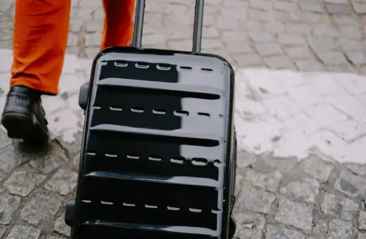 Błyszcząca, czarna walizka, idealna jako bagaż podręczny Ryanair, ciągnięta po bruku.