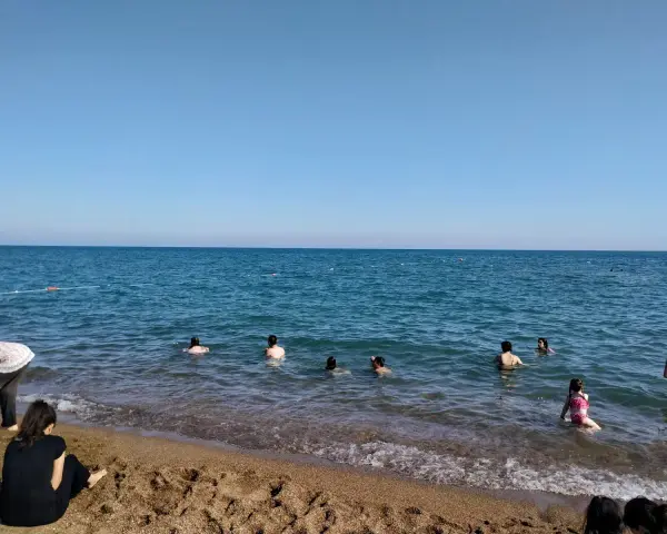 Słoneczny dzień na plaży Lara. Ludzie kąpią się w turkusowym morzu, inni odpoczywają na piaszczystym brzegu.