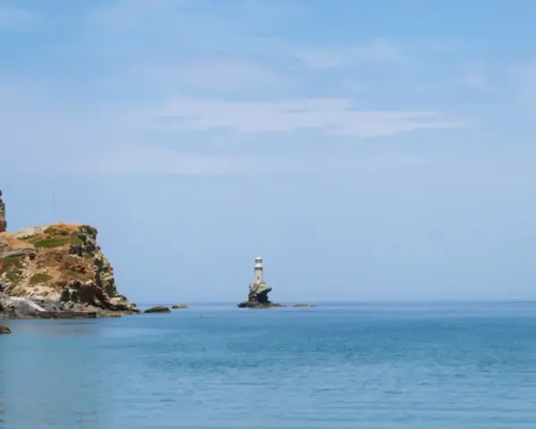 Widok na morze z latarnią morską na skale i zabudowaniami na klifie na wyspie Andros.