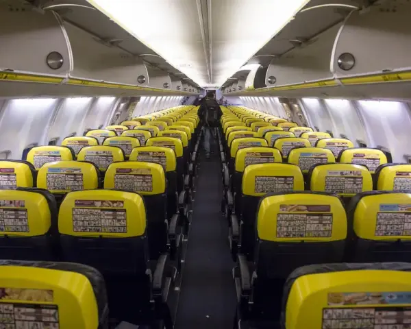 Puste rzędy żółtych siedzeń w samolocie Ryanair. Widać instrukcje bezpieczeństwa na oparciach.