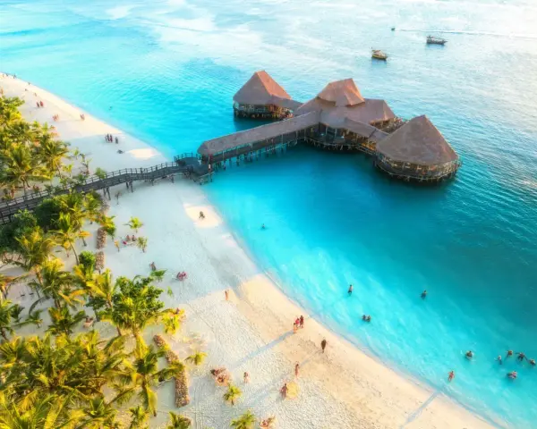 Rajska plaża na Zanzibarze z palmami i restauracją na wodzie. Sprawdź Zanzibar ceny, by zaplanować wymarzone wakacje.