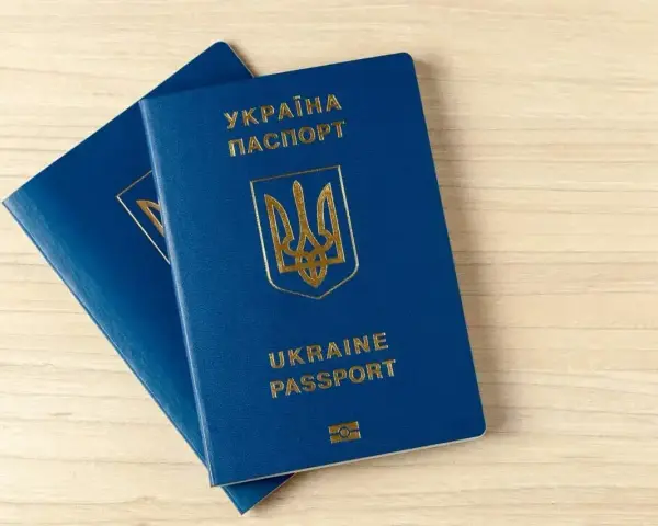 Dwa niebieskie paszporty biometryczne Ukrainy z złotym godłem i napisami leżą na drewnianym blacie.