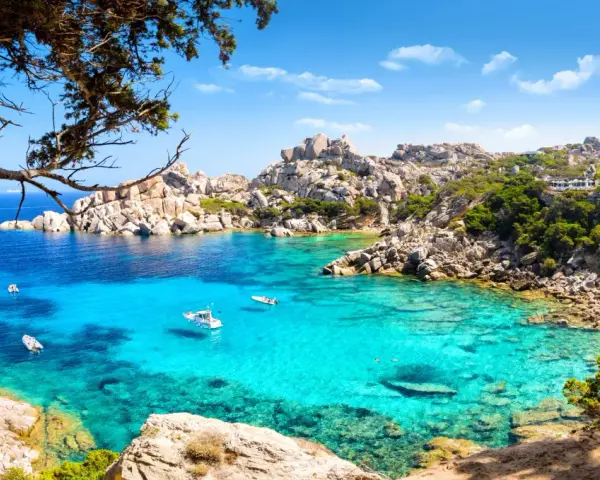 Turkusowa zatoka Costa Smeralda z łodziami i skalistym wybrzeżem.