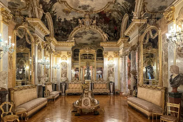 Złocone wnętrze pałacowe, przypominające muzeum w Madrycie, z malowidłami na suficie i bogatymi zdobieniami.