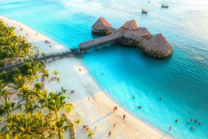 Rajska plaża na Zanzibarze z palmami i restauracją na wodzie. Sprawdź Zanzibar ceny, by zaplanować wymarzone wakacje.
