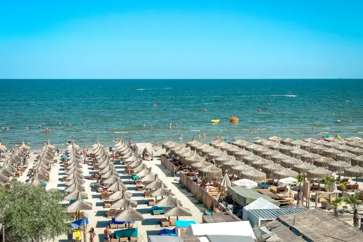 Słoneczna plaża w Rumunii, pełna leżaków i parasoli. Ludzie kąpią się w morzu, idealne miejsce na wakacje.