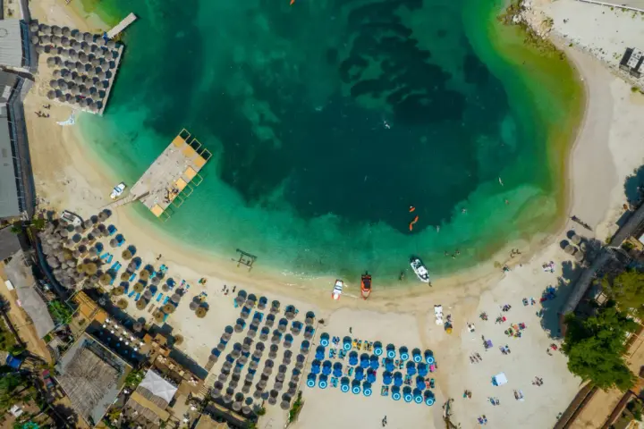 Widok z lotu ptaka na turkusowe morze i piaszczyste **albania plaże** z leżakami, parasolami i ludźmi cieszącymi się słońcem.