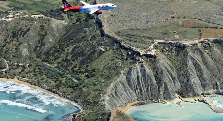 Samolot linii Malta Air przelatuje nad malowniczym wybrzeżem. Widok z lotu ptaka na maltańskie lotniska i krajobraz.