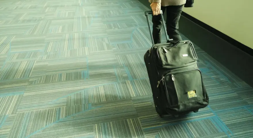Osoba ciągnie czarną walizkę Smartwings po lotniskowym chodniku z geometrycznym wzorem.