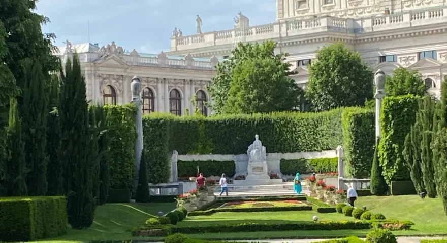 Wiedeń co zobaczyć: piękny ogród z rzeźbą i architekturą w tle.