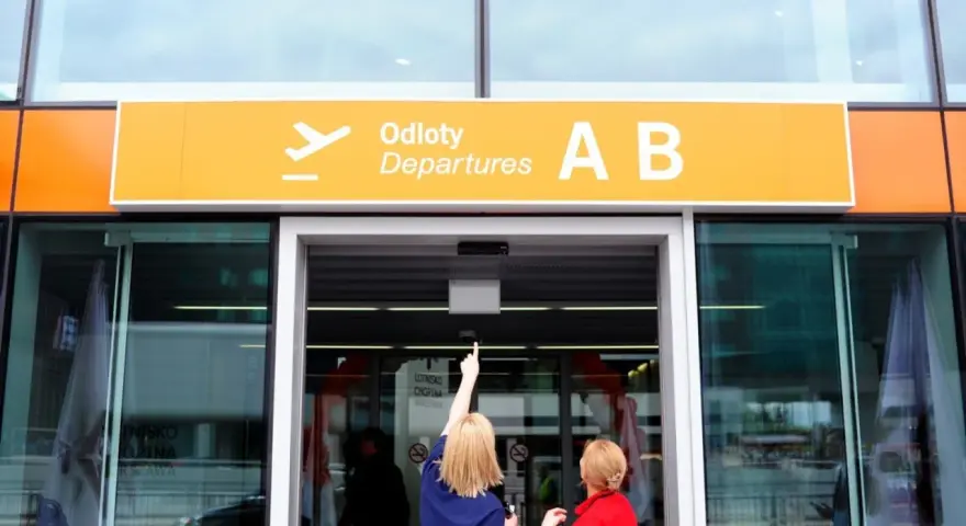 Dwie kobiety patrzą na tablicę "Odlocoty A B" na Lotnisku Chopina. Zastanawiają się, ile kosztuje parking na lotnisku Chopina.