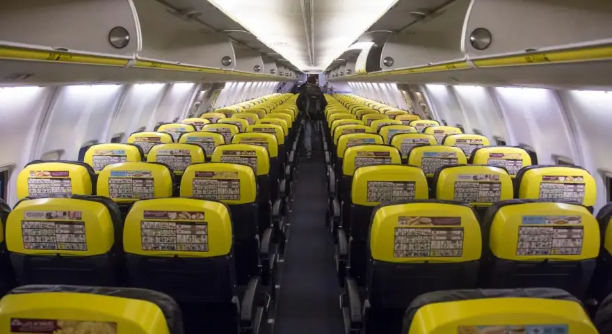 Puste rzędy żółtych siedzeń w samolocie Ryanair. Widać instrukcje bezpieczeństwa na oparciach.