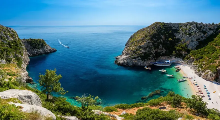 Malownicza zatoka z krystalicznie czystą wodą, plażą i łodziami. Idealne miejsce na wczasy samolotem all inclusive w Albanii.