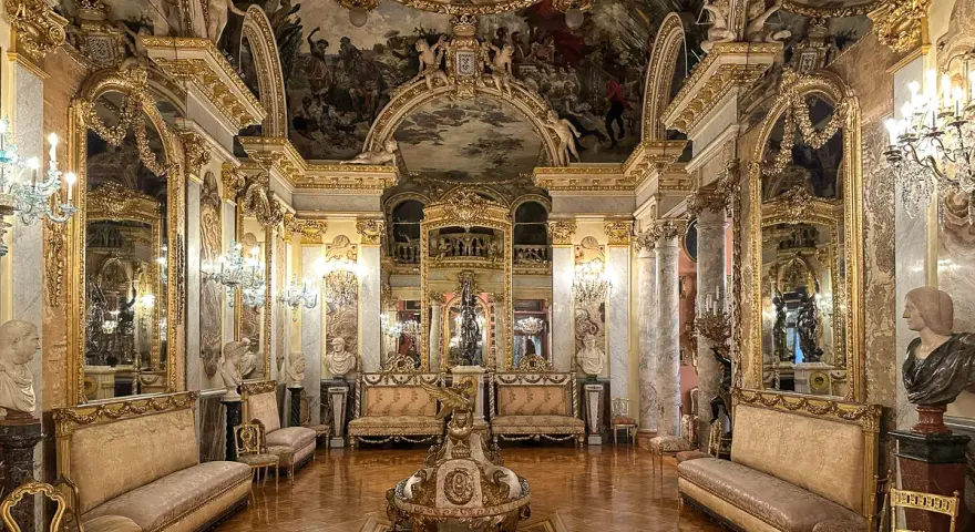Złocone wnętrze pałacowe, przypominające muzeum w Madrycie, z malowidłami na suficie i bogatymi zdobieniami.
