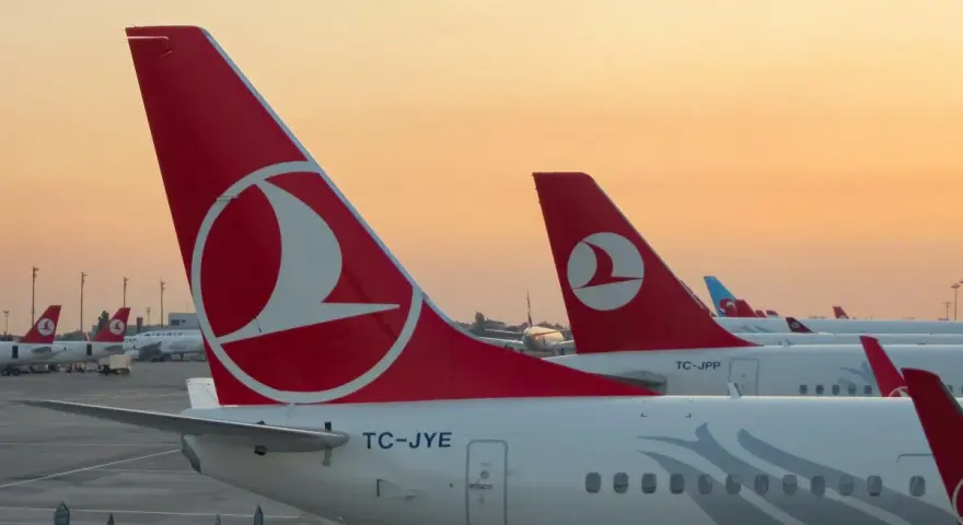 Samoloty tureckich linii lotniczych Turkish Airlines stojące na płycie lotniska o zachodzie słońca.