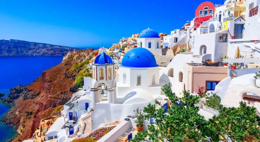 Santorini wakacje: białe domy z niebieskimi kopułami na zboczu klifu nad lazurowym morzem. Idealne miejsce na wymarzone wakacje.